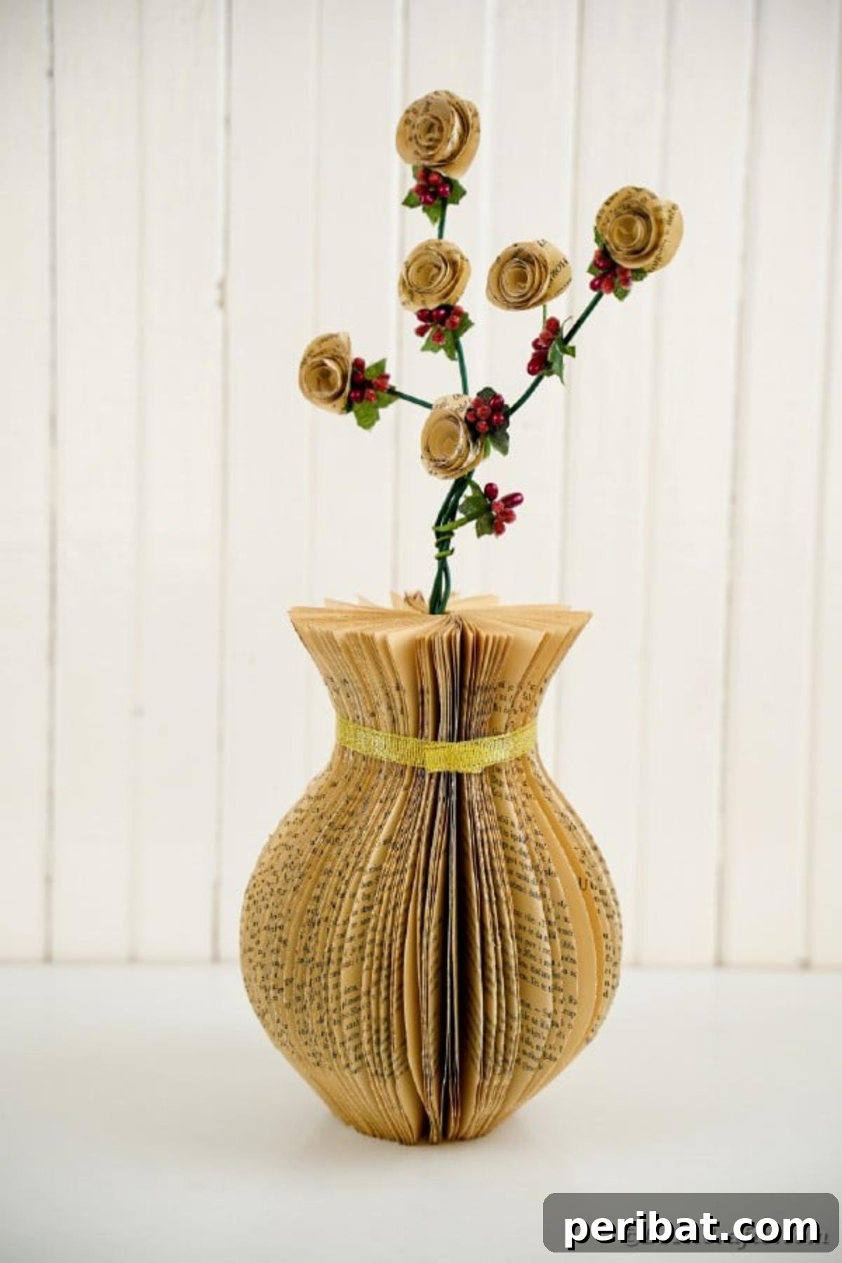 An elegant paper vase, crafted from old book pages, standing against a crisp white shiplap wall, highlighting its rustic texture and clean lines in a modern farmhouse setting.