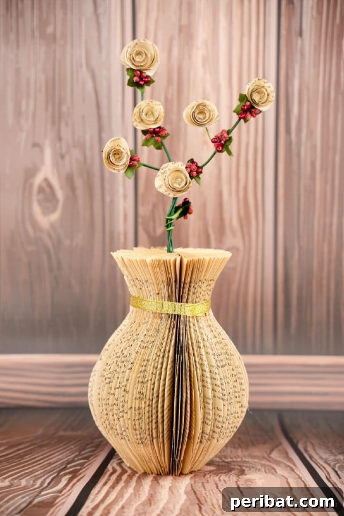 A unique paper vase, fashioned from the pages of an old book, showcasing its detailed construction against a warm wooden background, perfect for rustic decor.