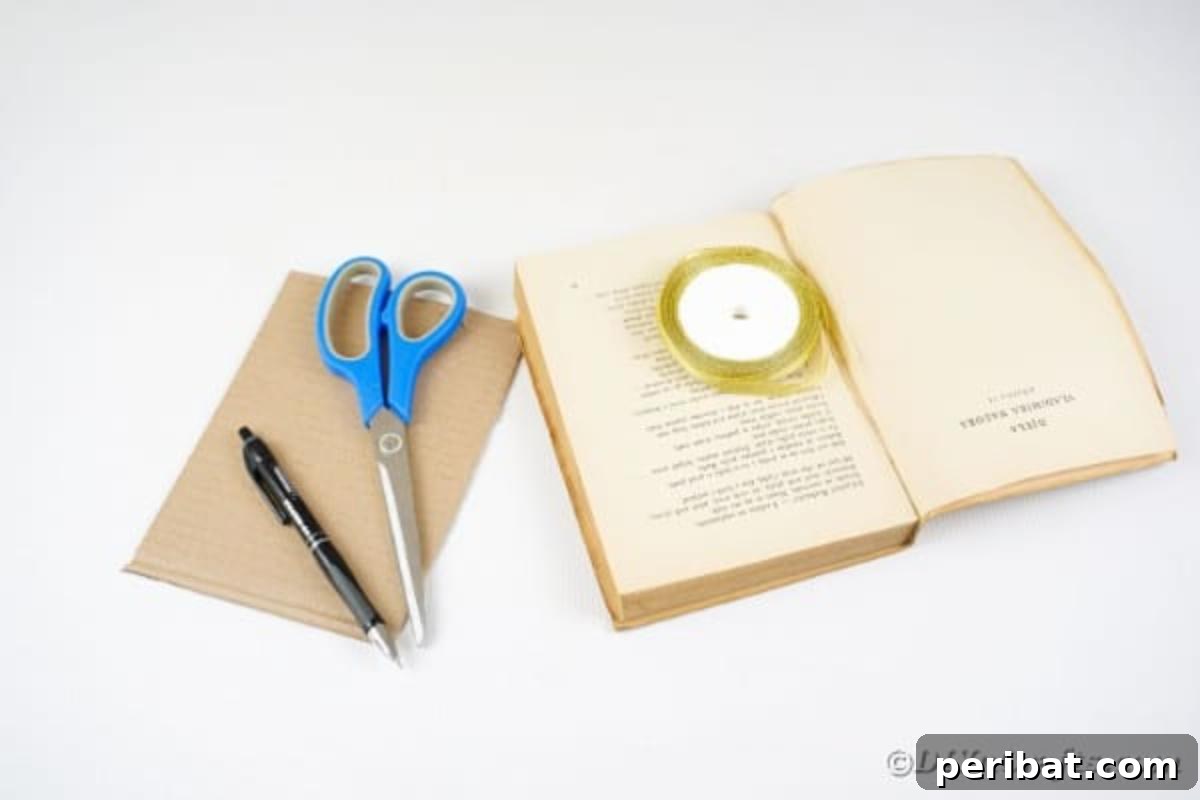 An array of craft supplies laid out on a table, including an old book, a craft knife, glue sticks, and ribbon, ready for making a paper vase.