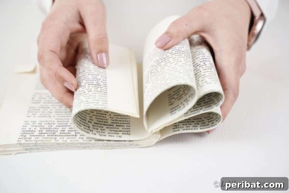 Storybook Pumpkin Charm 11 Hands rolling sections of book pages inward towards the spine, forming the initial curved segments of the pumpkin.