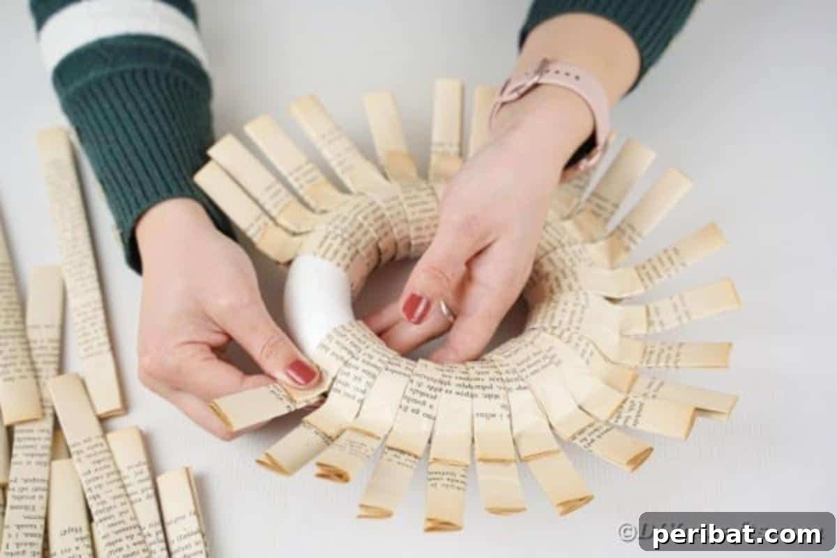 Multiple strips of folded paper meticulously glued onto a wreath form, building the first layer of the wreath.