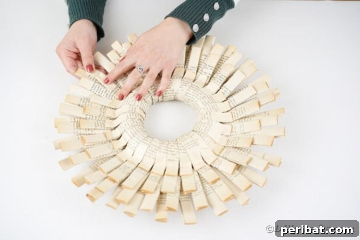 A new folded paper strip is being glued into the gaps on the backside of the wreath, creating a fuller, more layered look.