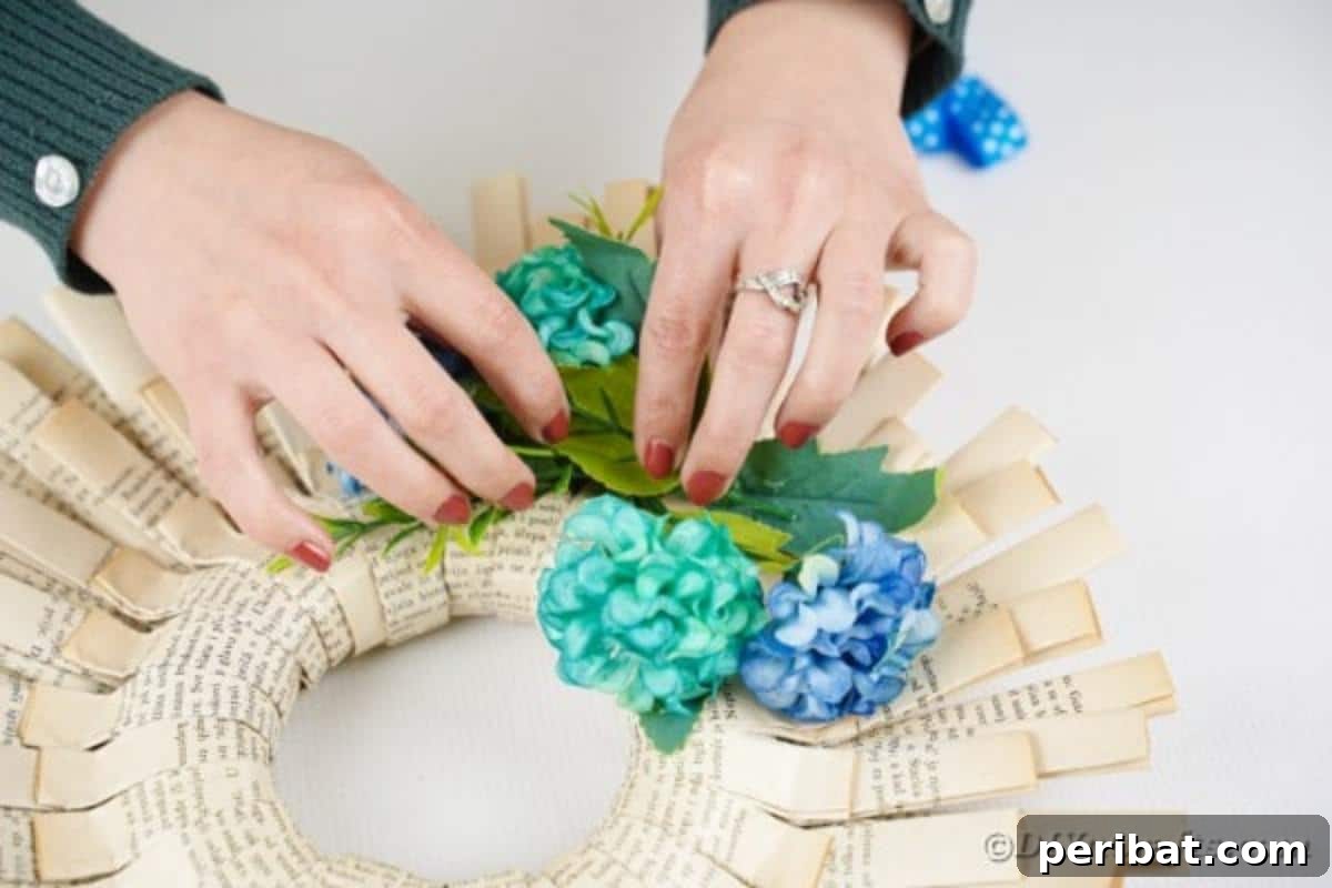 Delicate blue artificial flowers are being carefully placed and glued onto the surface of a finished paper wreath.