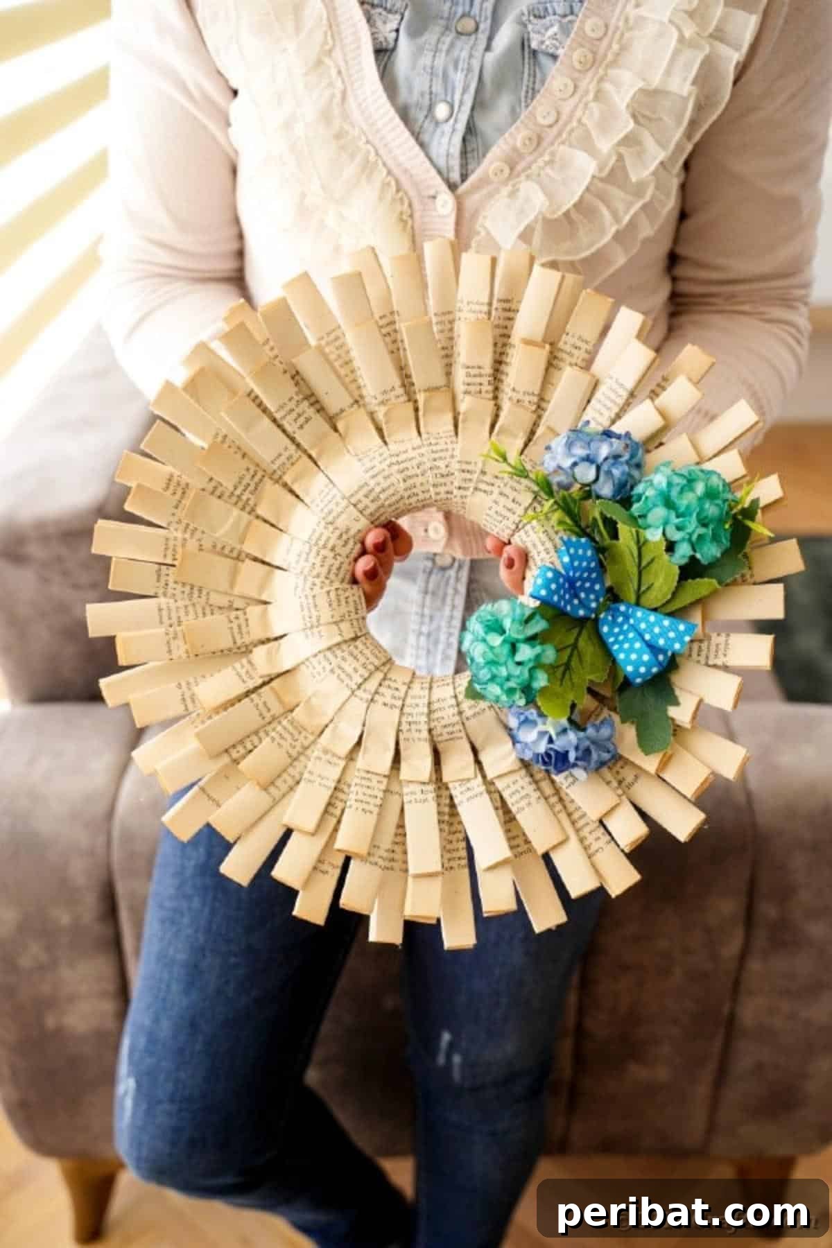 A woman proudly holds up a finished, intricately folded paper wreath, showcasing her successful DIY craft project.