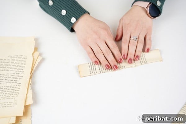 A piece of paper, already folded once, being folded in half again to create a narrower strip.