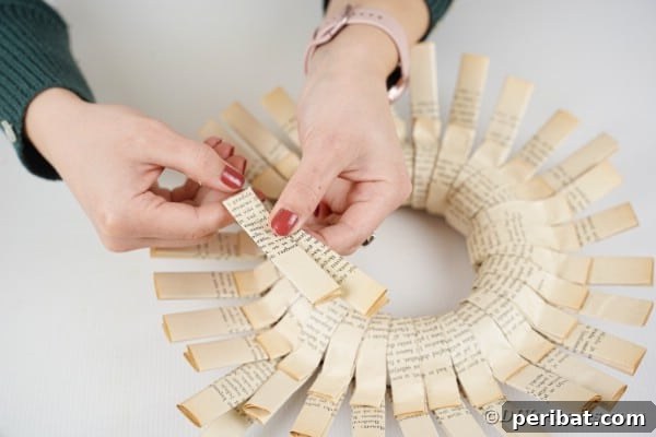 A folded paper strip is being bent at an angle, preparing it to be added as a second, textured layer to the wreath.