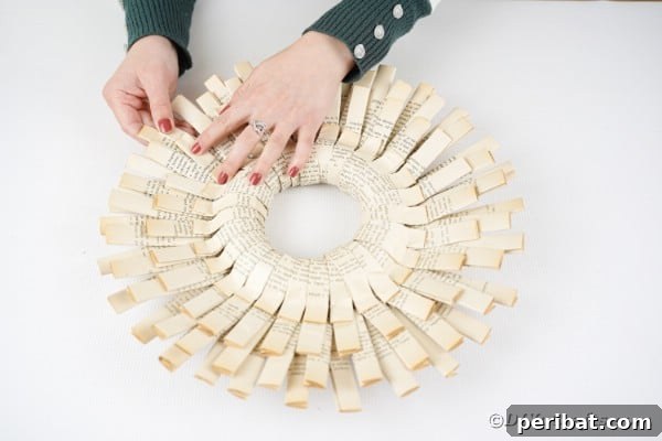A new folded paper strip is being glued into the gaps on the backside of the wreath, creating a fuller, more layered look.