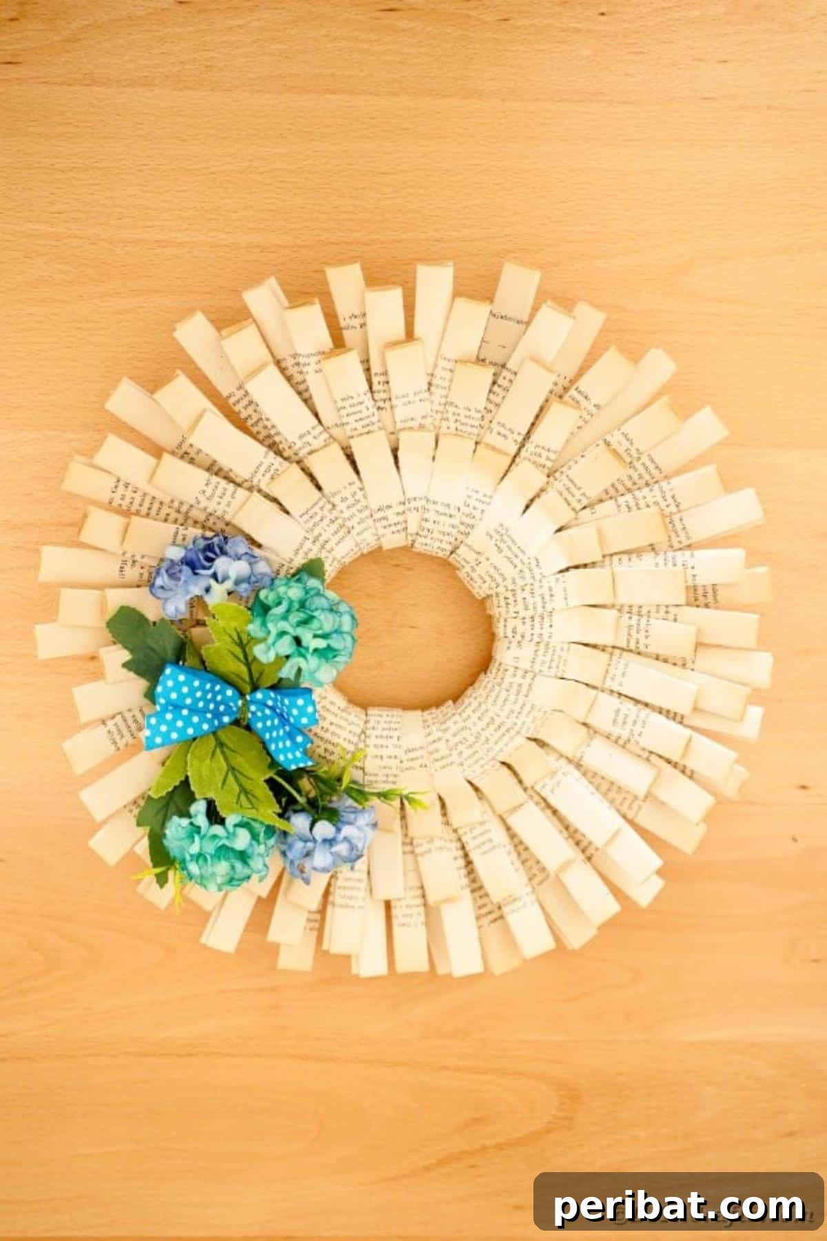 A beautifully textured paper wreath, crafted from folded book pages, rests on a smooth beige surface, highlighting its intricate design.