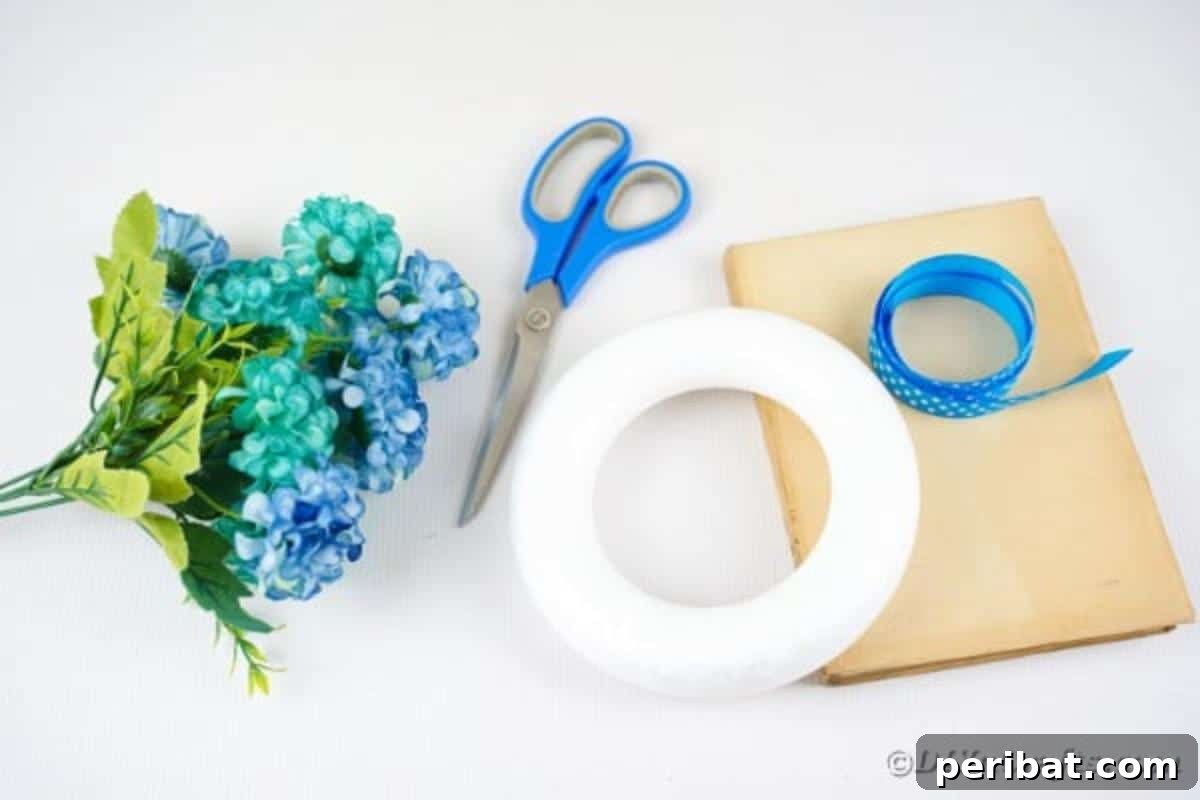 A neat arrangement of crafting supplies for a folded paper wreath, including old book pages, a Styrofoam wreath form, ribbon, and artificial flowers.