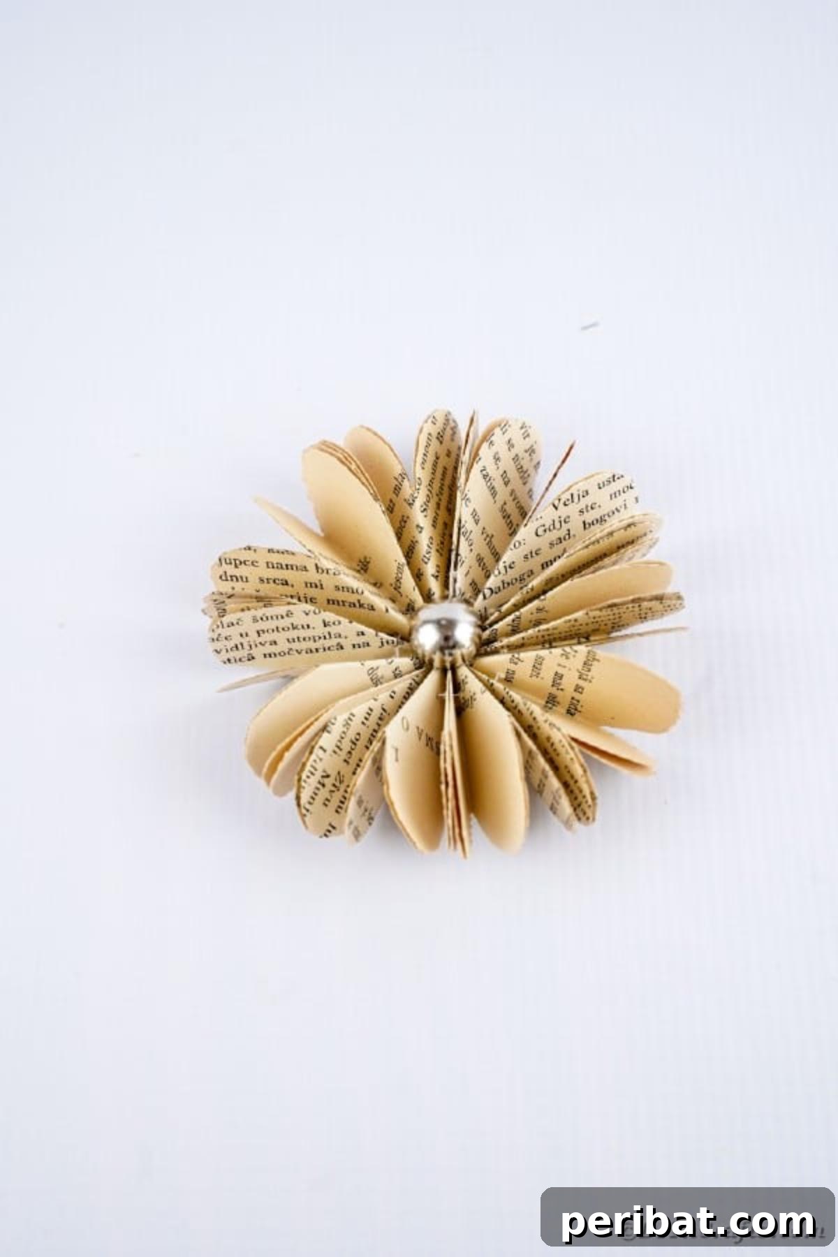 Charming Blooms from Repurposed Book Pages 22 A delicate old book page flower displayed on a clean white table, emphasizing its simple beauty