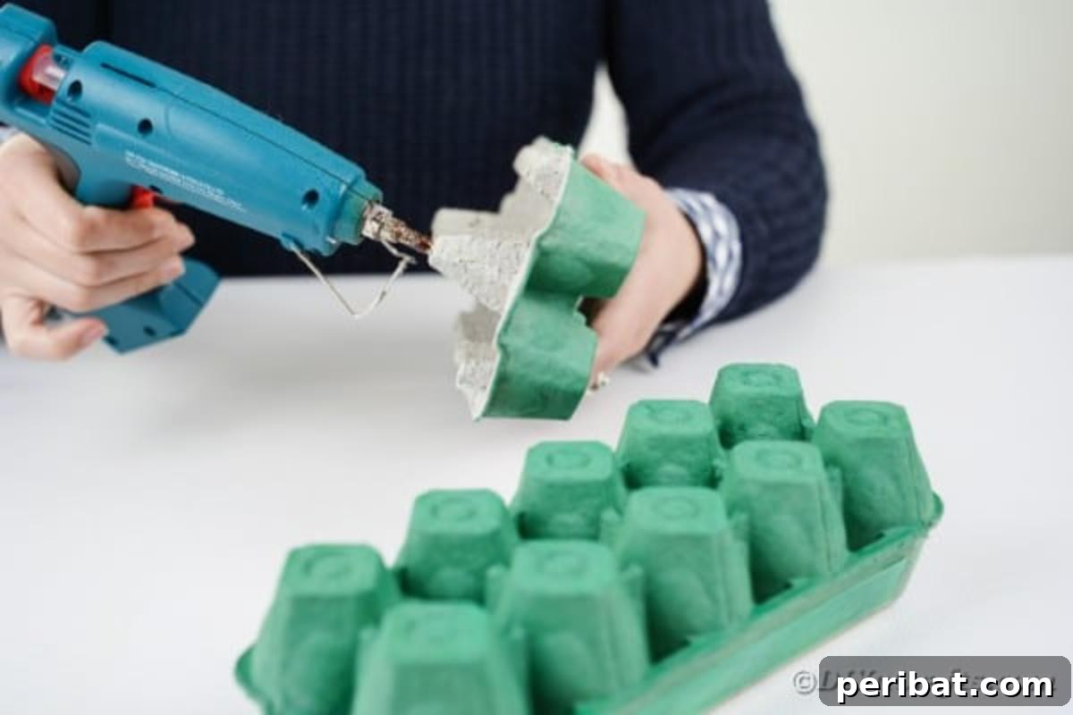Hands gluing two sections of a painted egg carton together, forming the dragon's body.