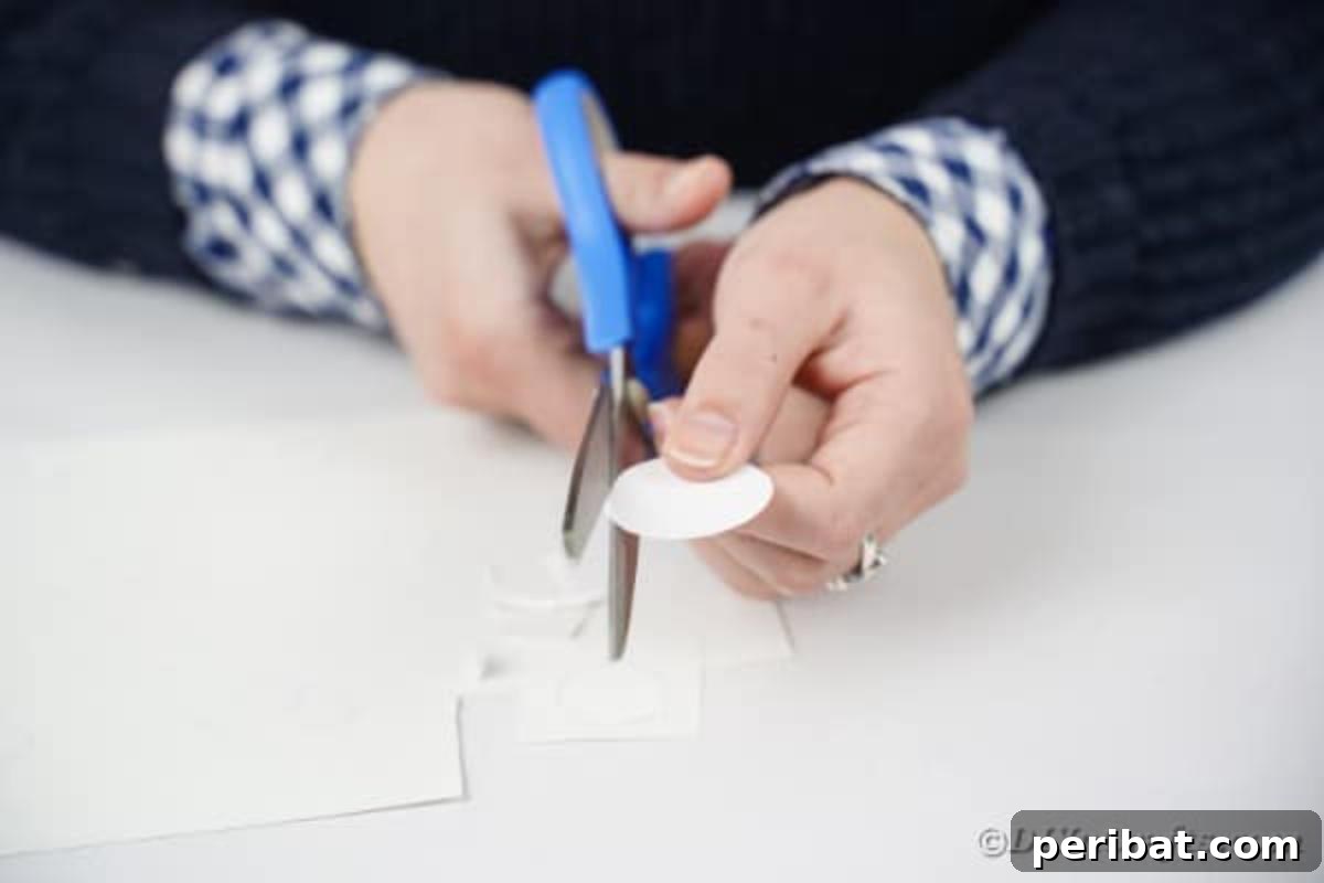 Hands cutting out white paper circles with scissors on a wooden table.