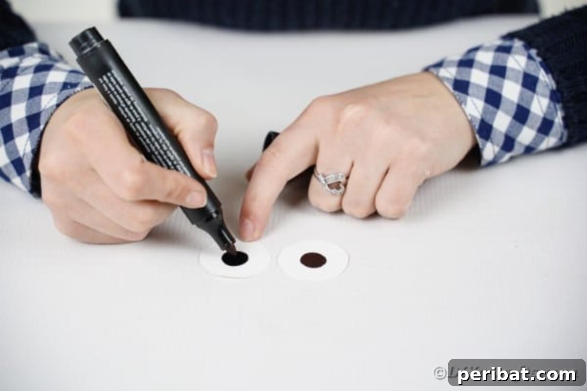 A hand drawing black circles onto the center of white paper circles with a marker.