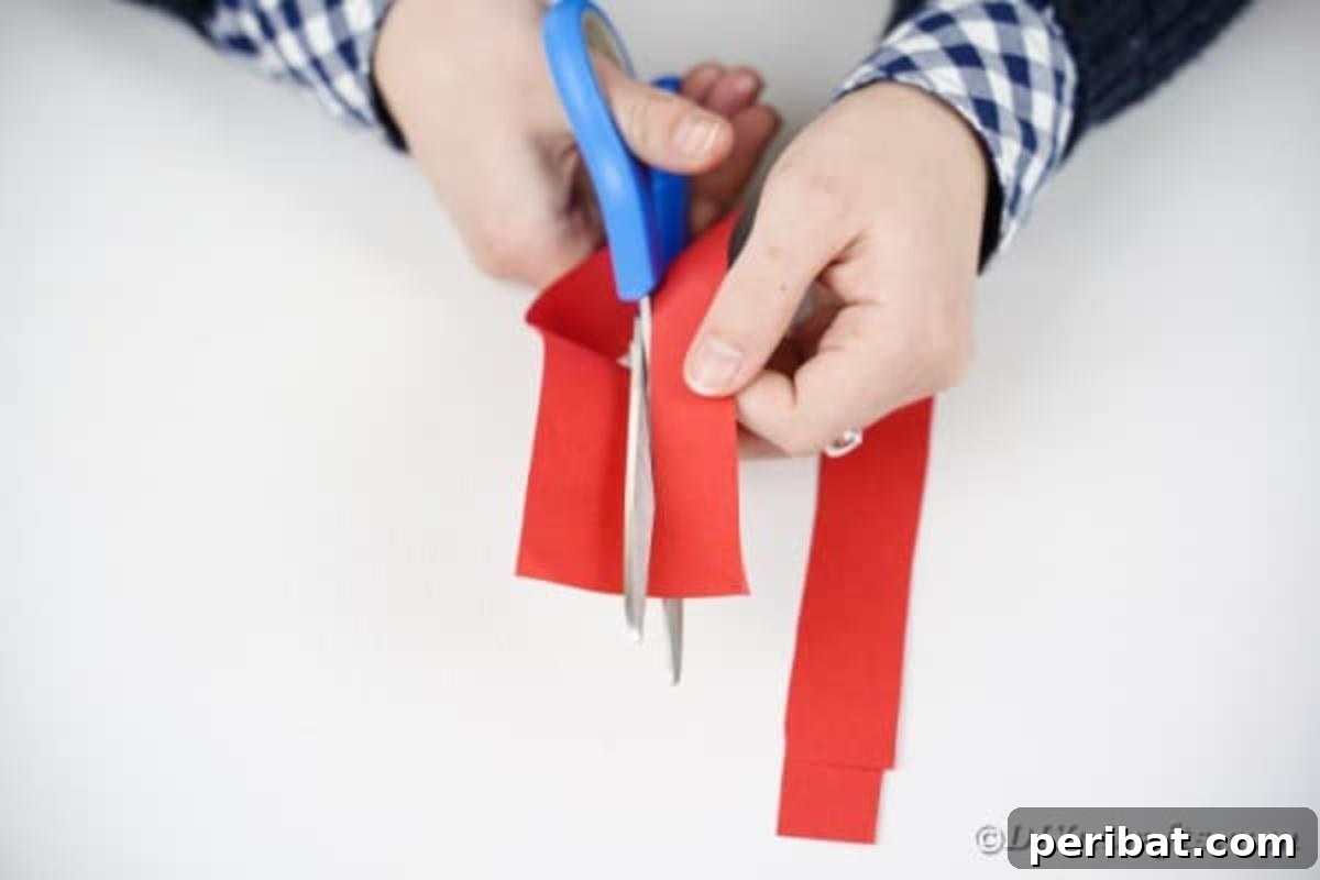 Hands cutting long strips of red paper with scissors.
