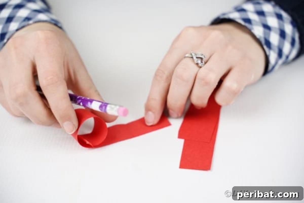 A hand using a pencil to roll one end of a red paper strip, creating a curl.