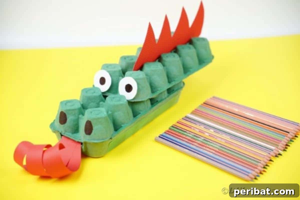 A finished green egg carton dragon with red details, sitting on a yellow table surface.