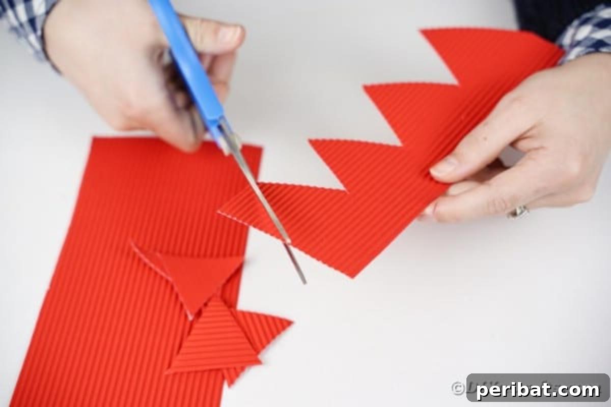 Hands cutting sharp triangles from a piece of red corrugated cardboard with scissors.
