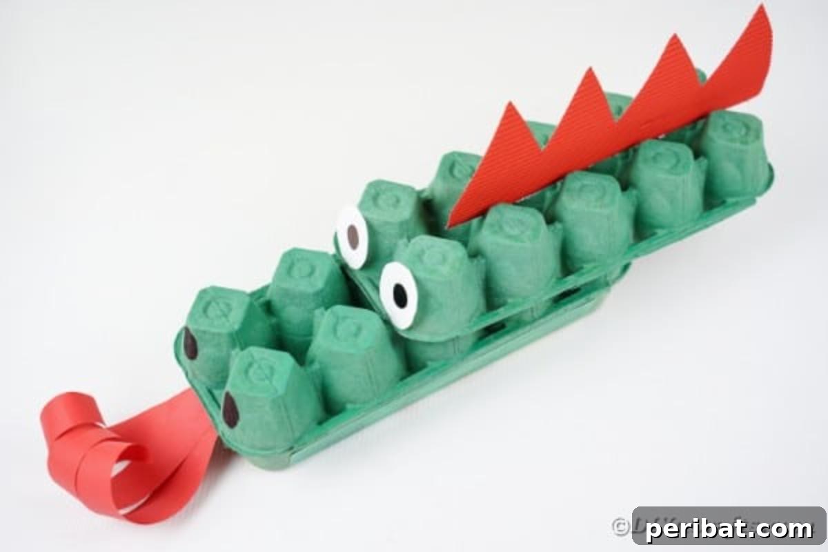 A finished green egg carton dragon with red spikes, sitting on a clean white table surface.