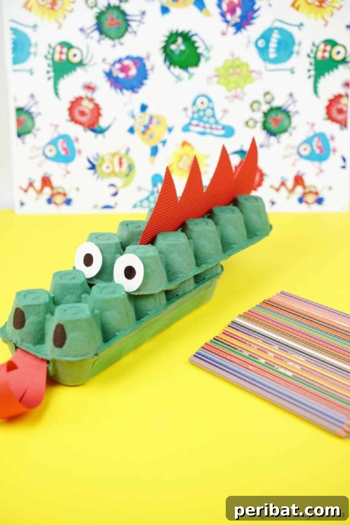 A finished green egg carton dragon with red spikes and eyes, resting on a yellow tabletop.