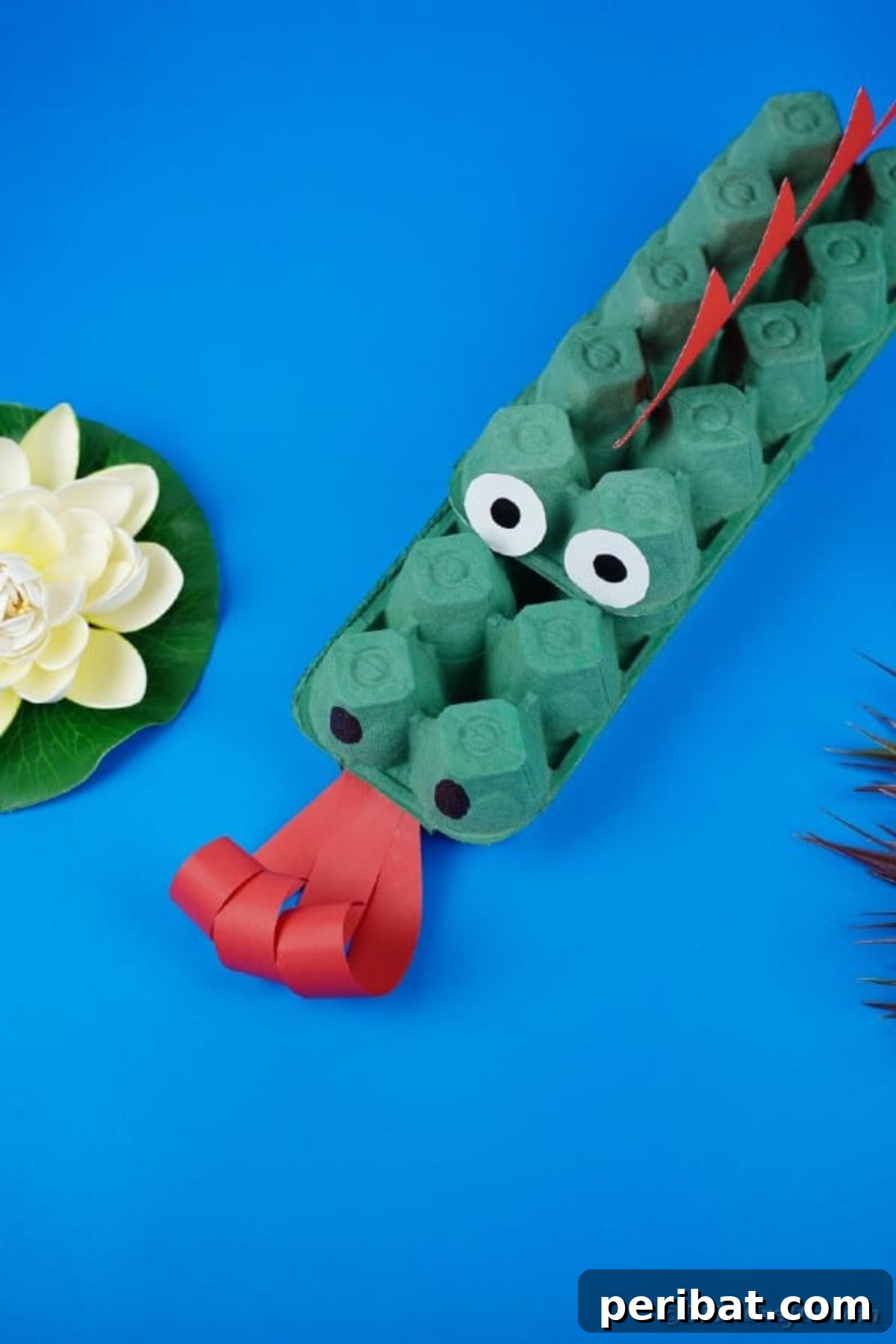 Another view of the green egg carton dragon, highlighting its construction and painted details on a blue surface.