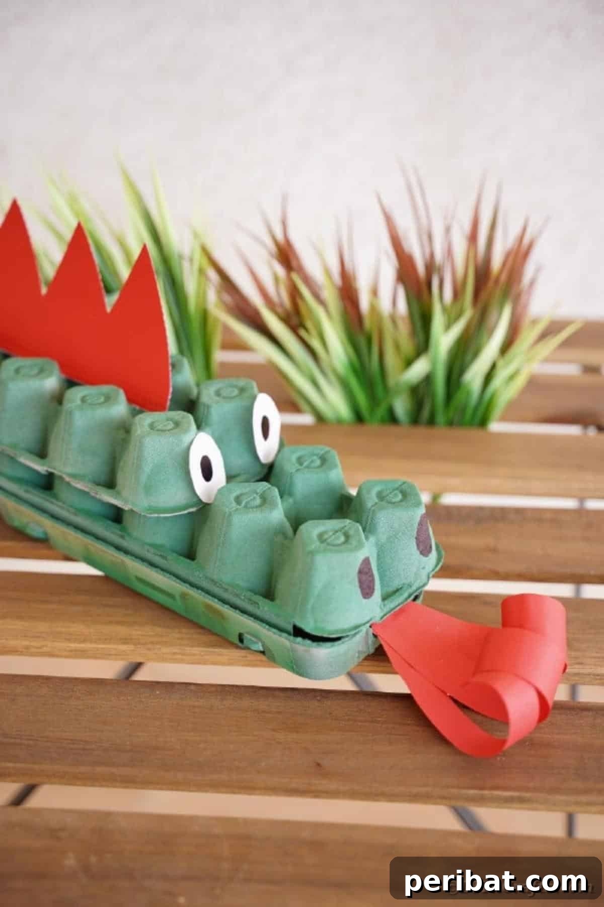 A close-up of the green egg carton dragon craft, displayed on a rustic wooden table, showing its textured body.