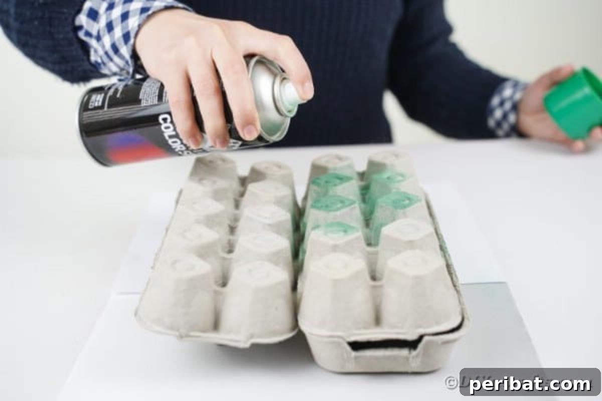 A hand spraying green paint onto an egg carton section placed on newspaper outdoors.