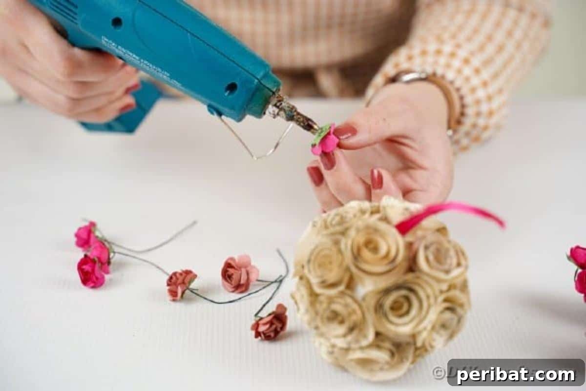 From Pages to Petals: DIY Book Rose Sphere 16 A crafter gluing miniature artificial roses into the gaps of a paper rose ball for added color and fullness