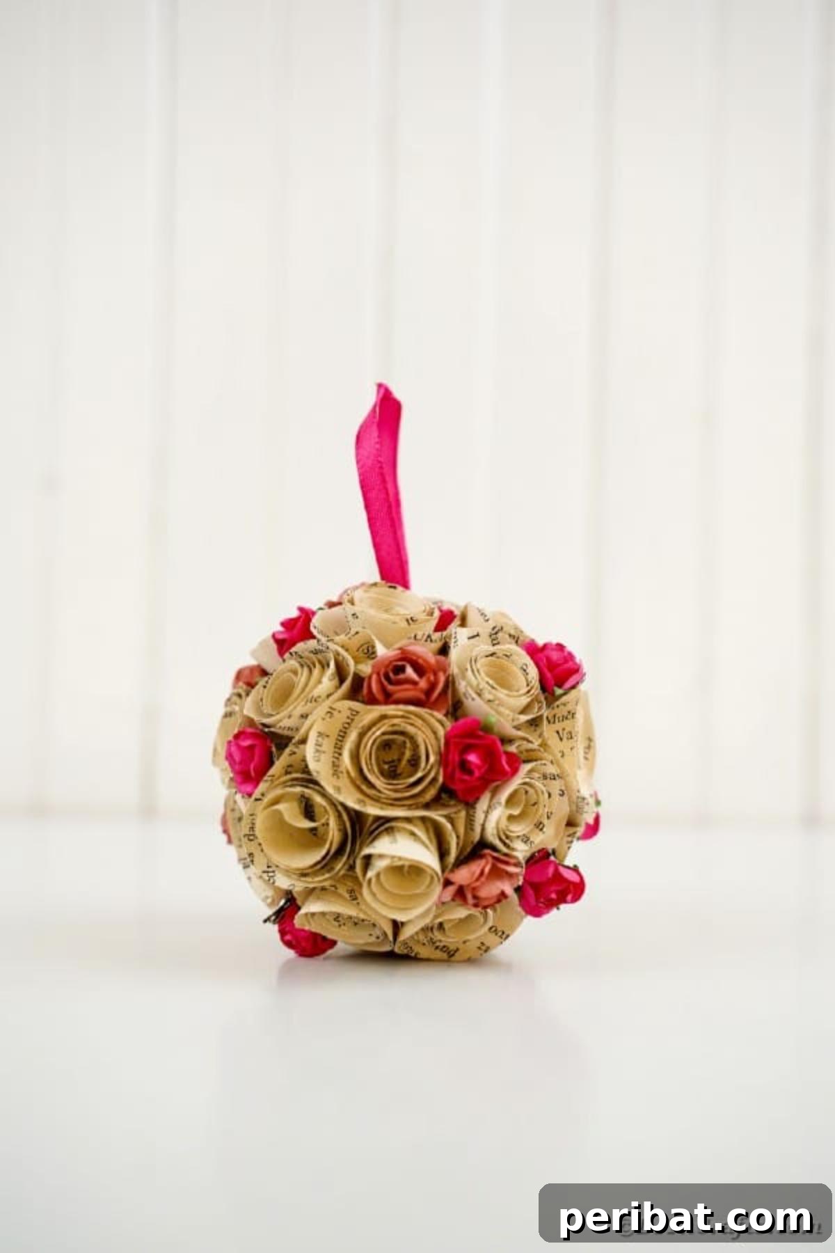 From Pages to Petals: DIY Book Rose Sphere 20 An elegant paper rose ball ornament hanging against a pristine white wooden wall