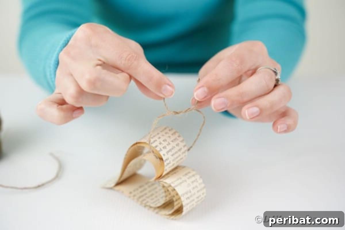 Heirloom Book Page Heart Bunting 15 Close-up of hands tying a small piece of twine through the top of a finished paper heart