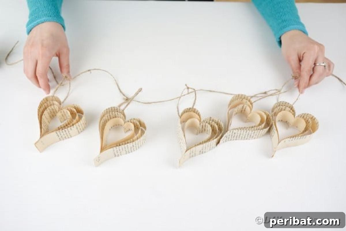 Heirloom Book Page Heart Bunting 16 Woman's hands arranging paper hearts onto a long piece of twine to create a banner