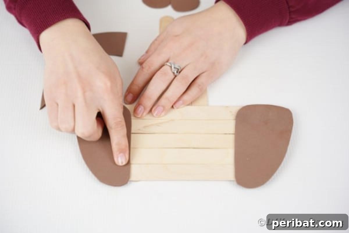 Gluing brown paper ears onto the craft stick dog's head
