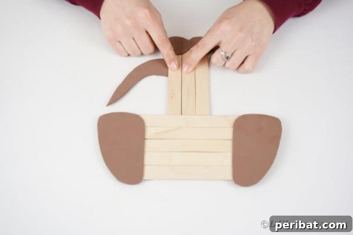 Gluing a brown paper tail onto the side of the popsicle stick dog