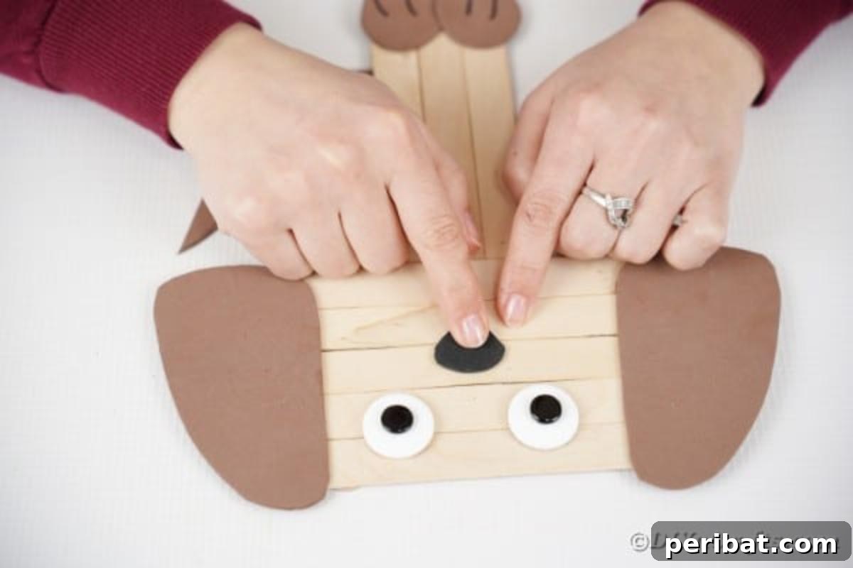 Attaching a black paper nose just below the craft stick puppy's eyes