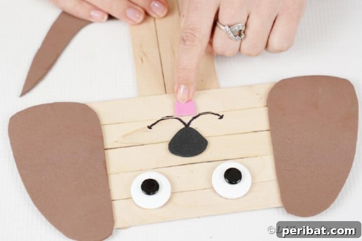 Adding a pink paper tongue just below the craft stick puppy's marker-drawn mouth