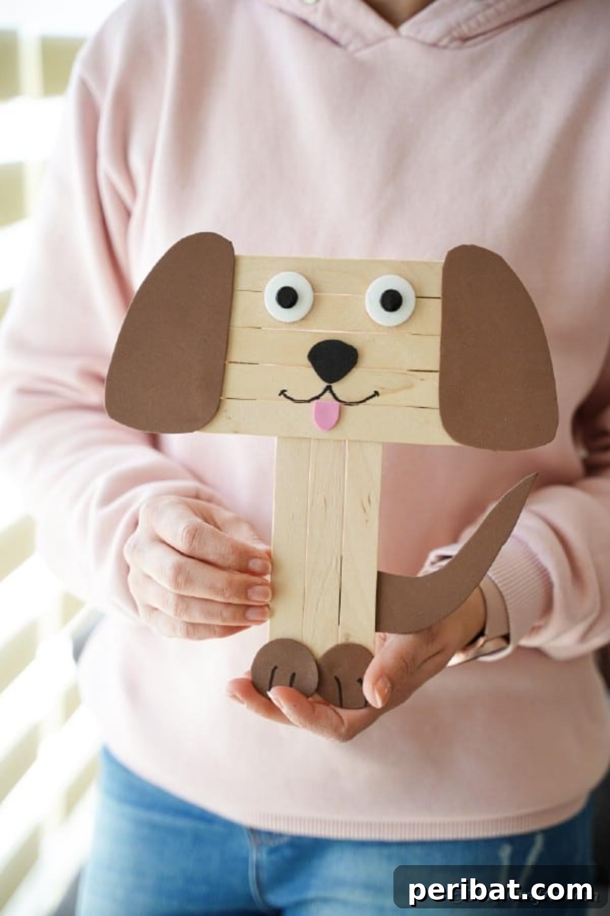 A finished craft stick dog held by a woman, showcasing personalization options
