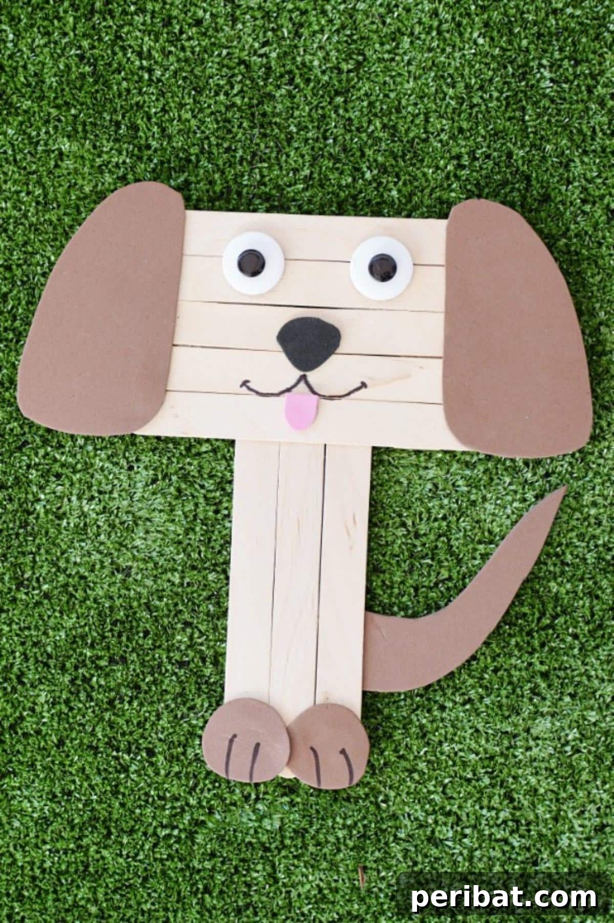 Playful craft stick puppy sitting on green grass