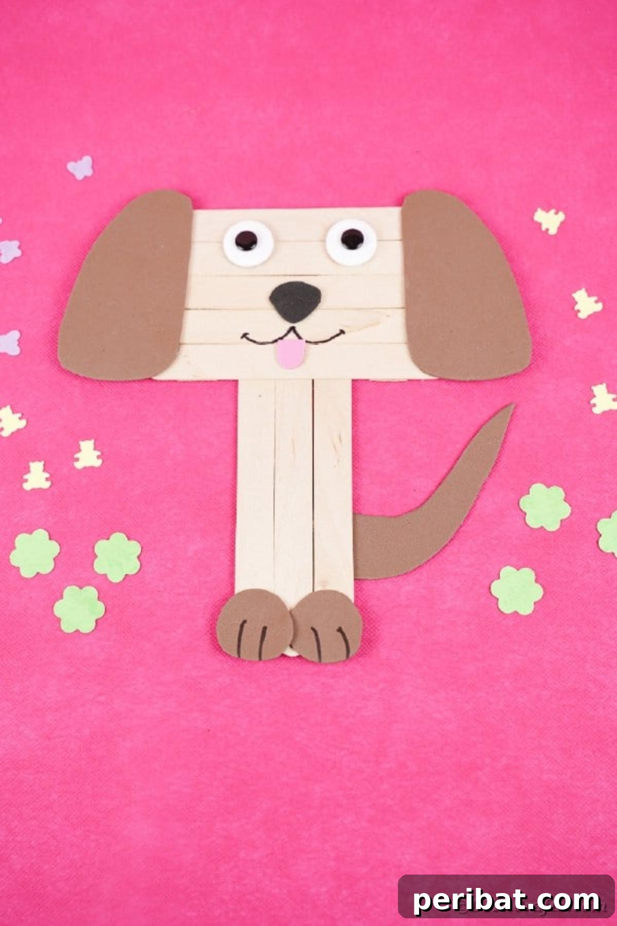 Close-up of a whimsical popsicle stick puppy on a pink surface