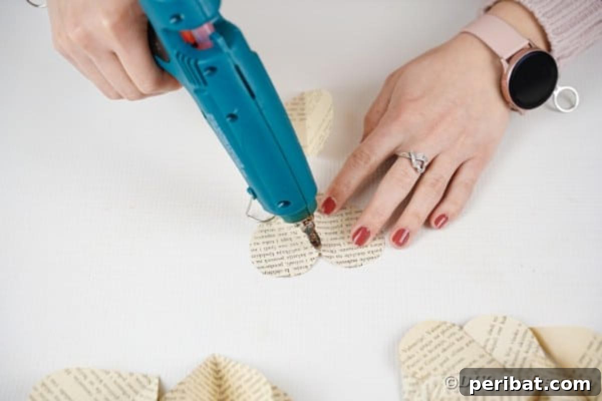 Adding a dab of hot glue to the fold of a paper heart for attaching to twine