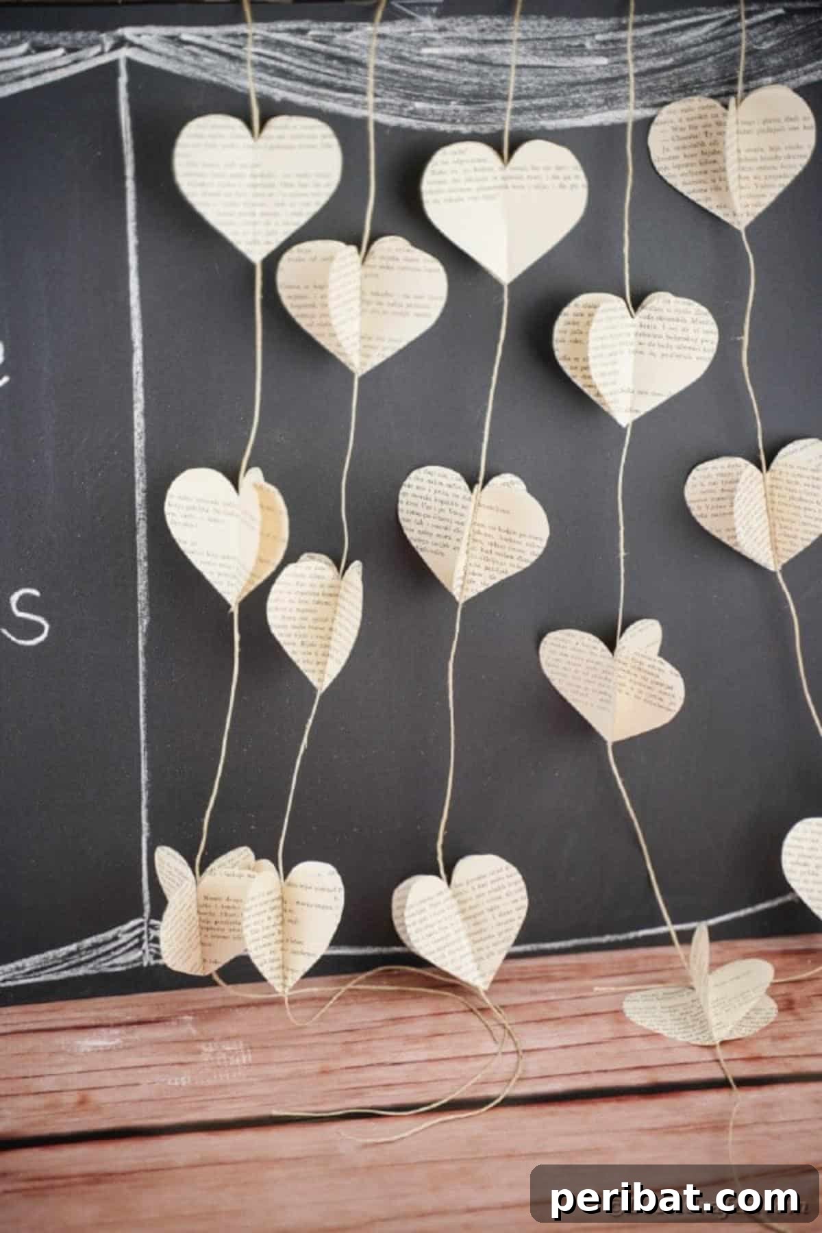 Finished paper heart garland from old book pages, hanging gracefully against a dark chalkboard background