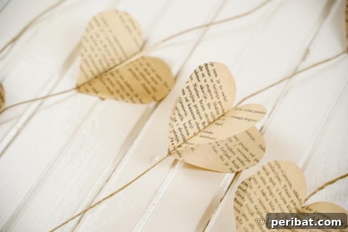 Close-up of a rustic paper heart garland made from old book pages, resting on a white wooden surface, showcasing its vintage charm
