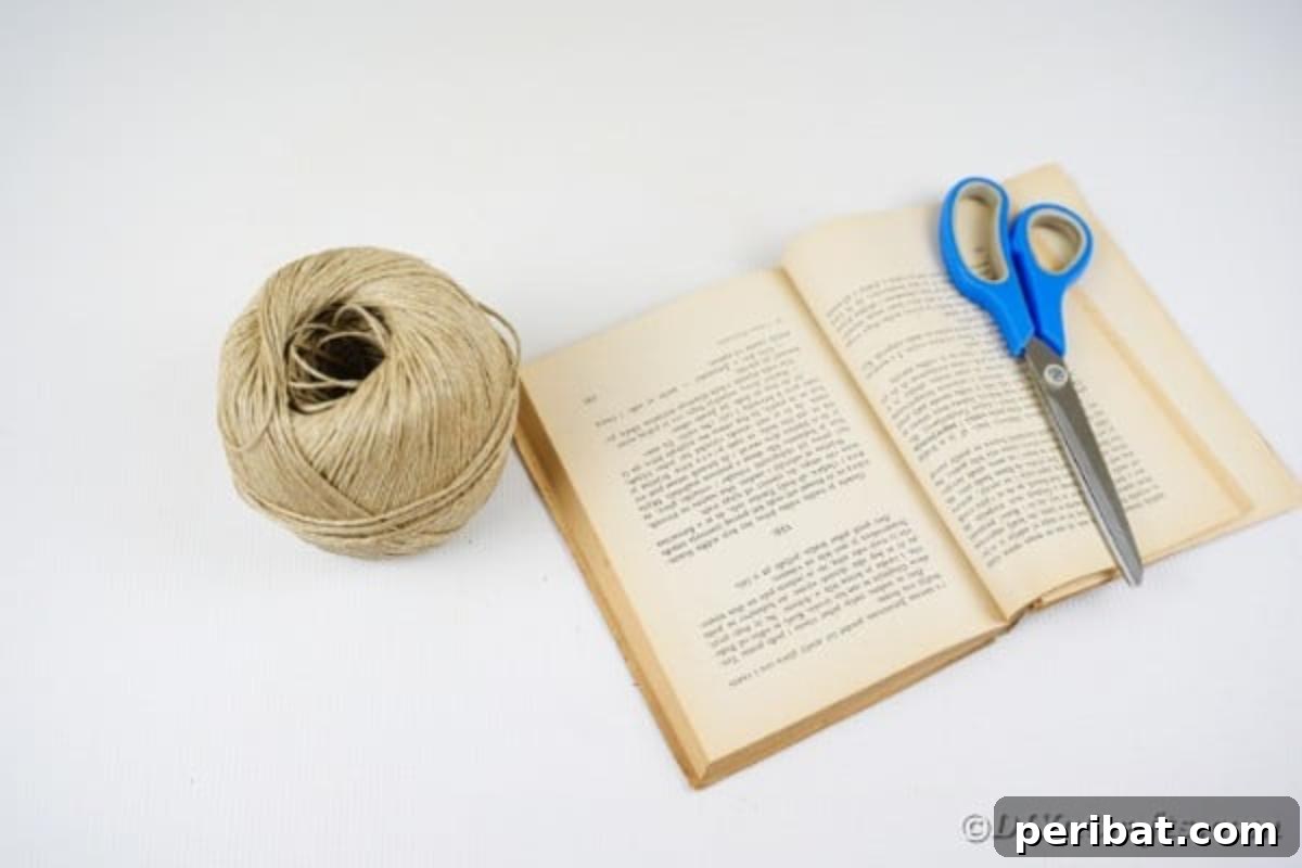 Craft supplies for making a paper heart garland, including old book pages, twine, scissors, and a hot glue gun with sticks