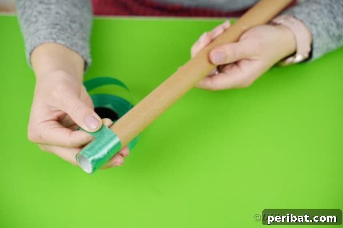 A hand meticulously wrapping a thin cardboard tube with a dark green ribbon, creating a uniform and attractive surface for the crane's arm.