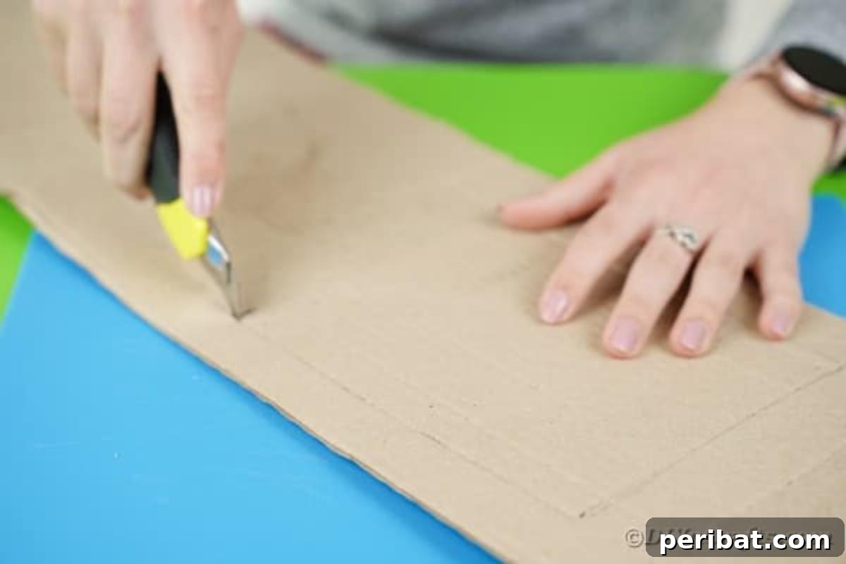 A craft knife precisely cutting out a square from the cardboard, creating the window aperture for the crane's cab.
