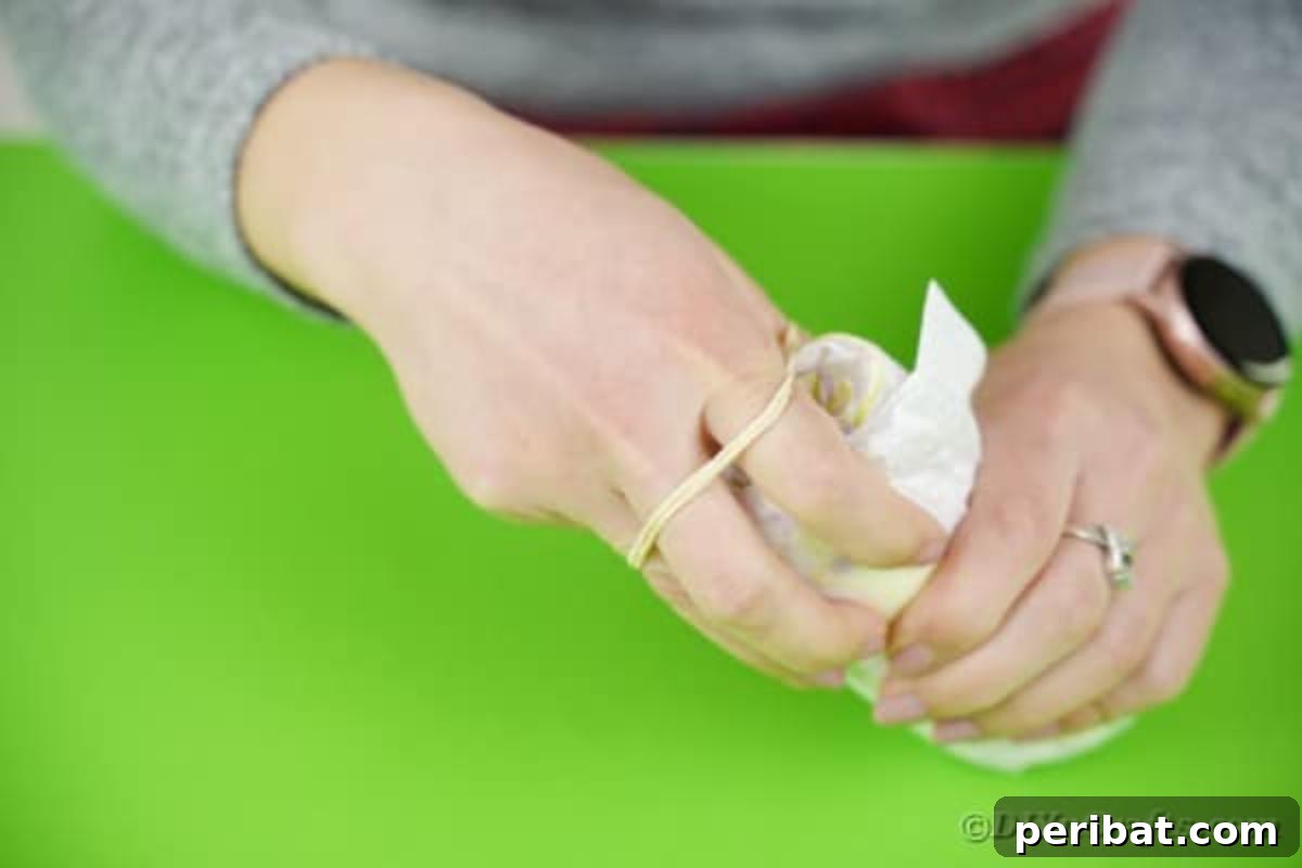 A rolled diaper being secured with a white rubber band, showing the essential step for preparing diapers to form the base of the crane cake.