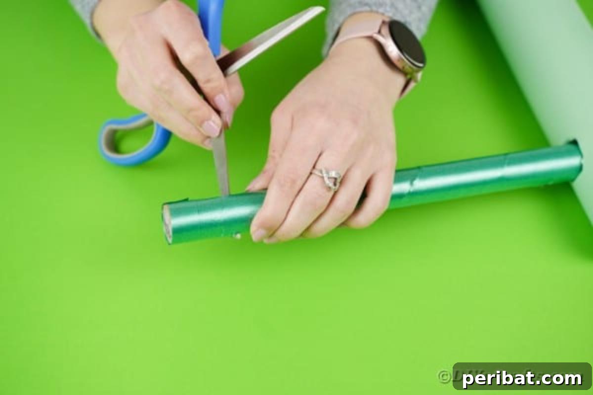 A hand using scissors to cut a small, neat hole into one end of the small cardboard tube, preparing it for the twine mechanism of the crane.