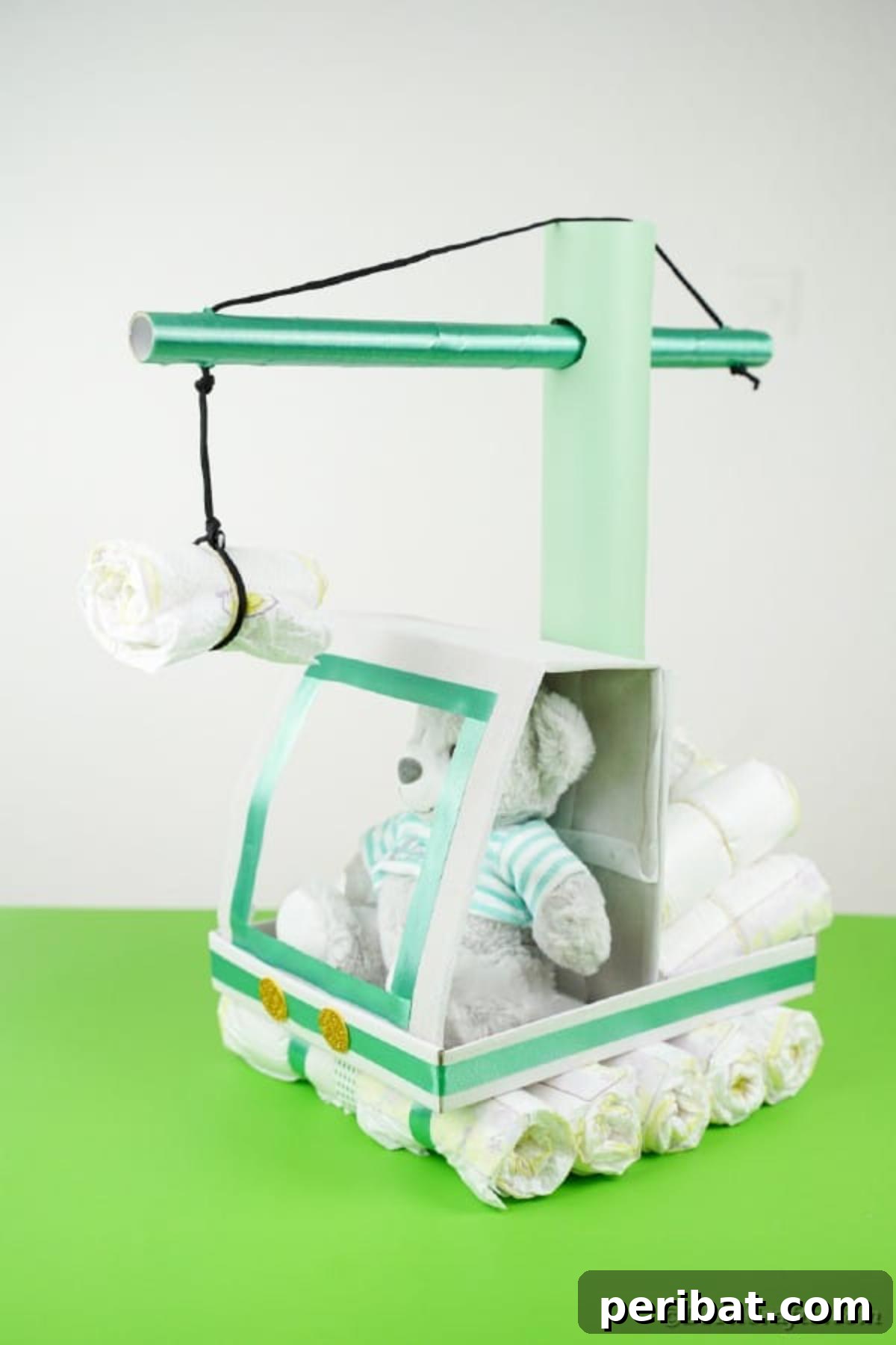 A finished crane diaper cake with a cute teddy bear 'operator' sitting on a green desk, illustrating its playful and decorative appeal.