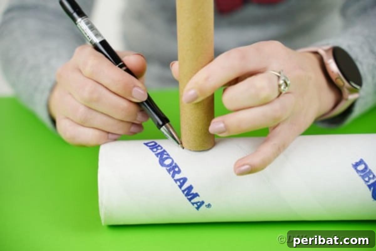Close-up of a hand tracing a circle onto a larger cardboard tube using a smaller tube as a guide, marking the spot for the crane's movable arm.