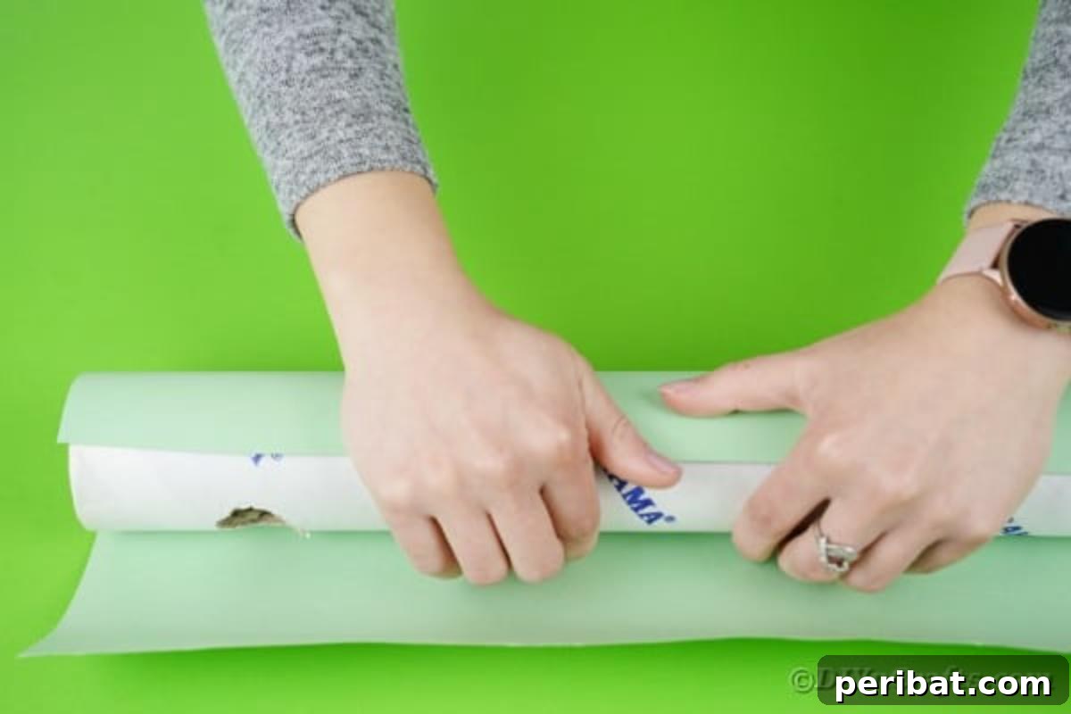 Hands carefully wrapping a cardboard tube with light-colored wrapping paper, ensuring a smooth and even finish to form part of the crane's structure.