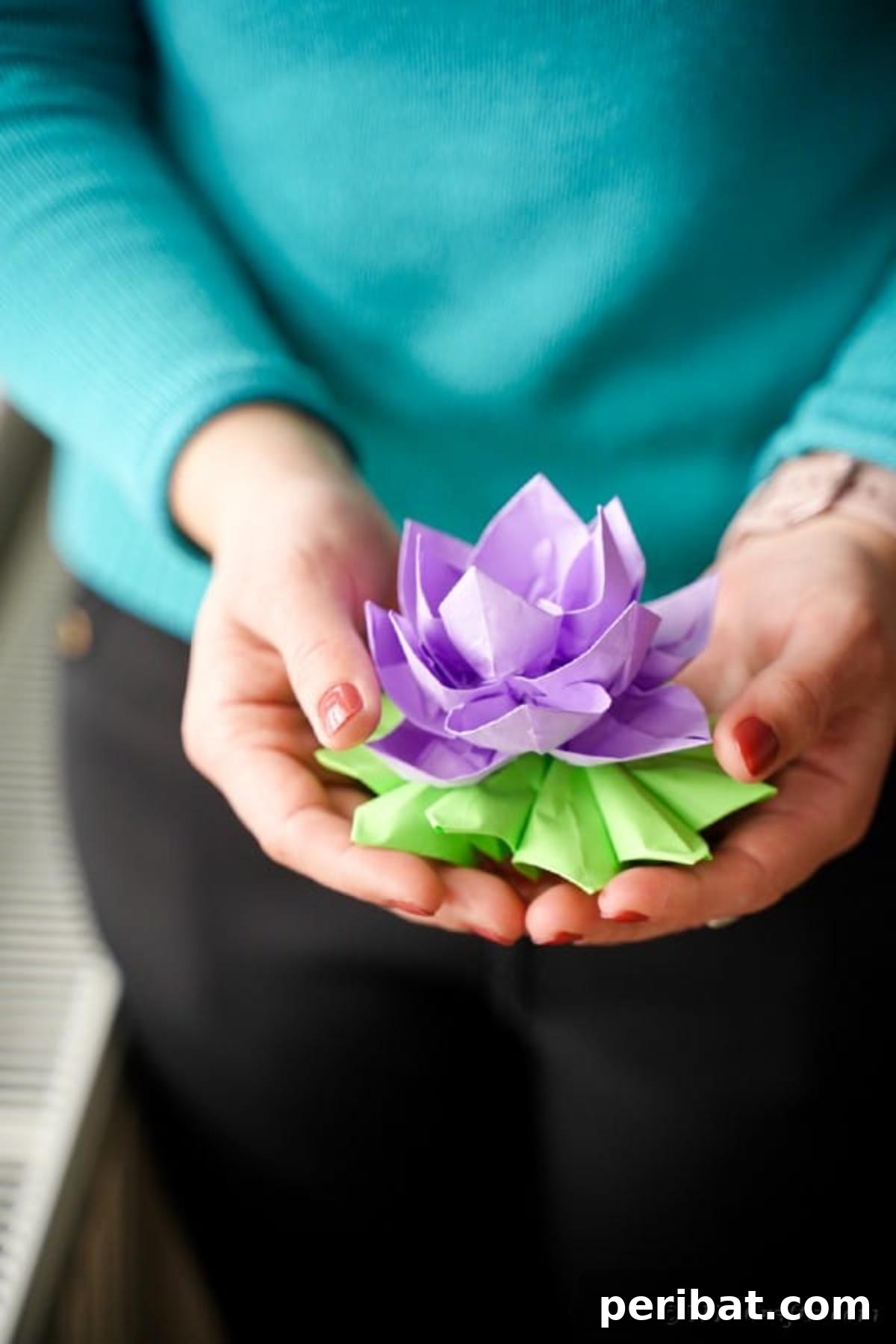 A crafter proudly holds up a finished purple paper lotus, demonstrating its beauty.