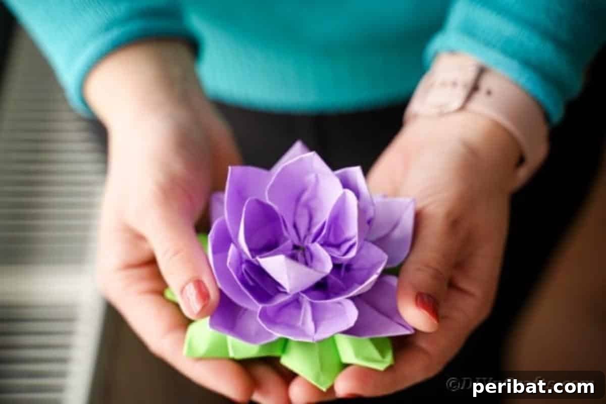 A person's hand gently holds a freshly crafted purple paper lotus, showcasing the finished product.